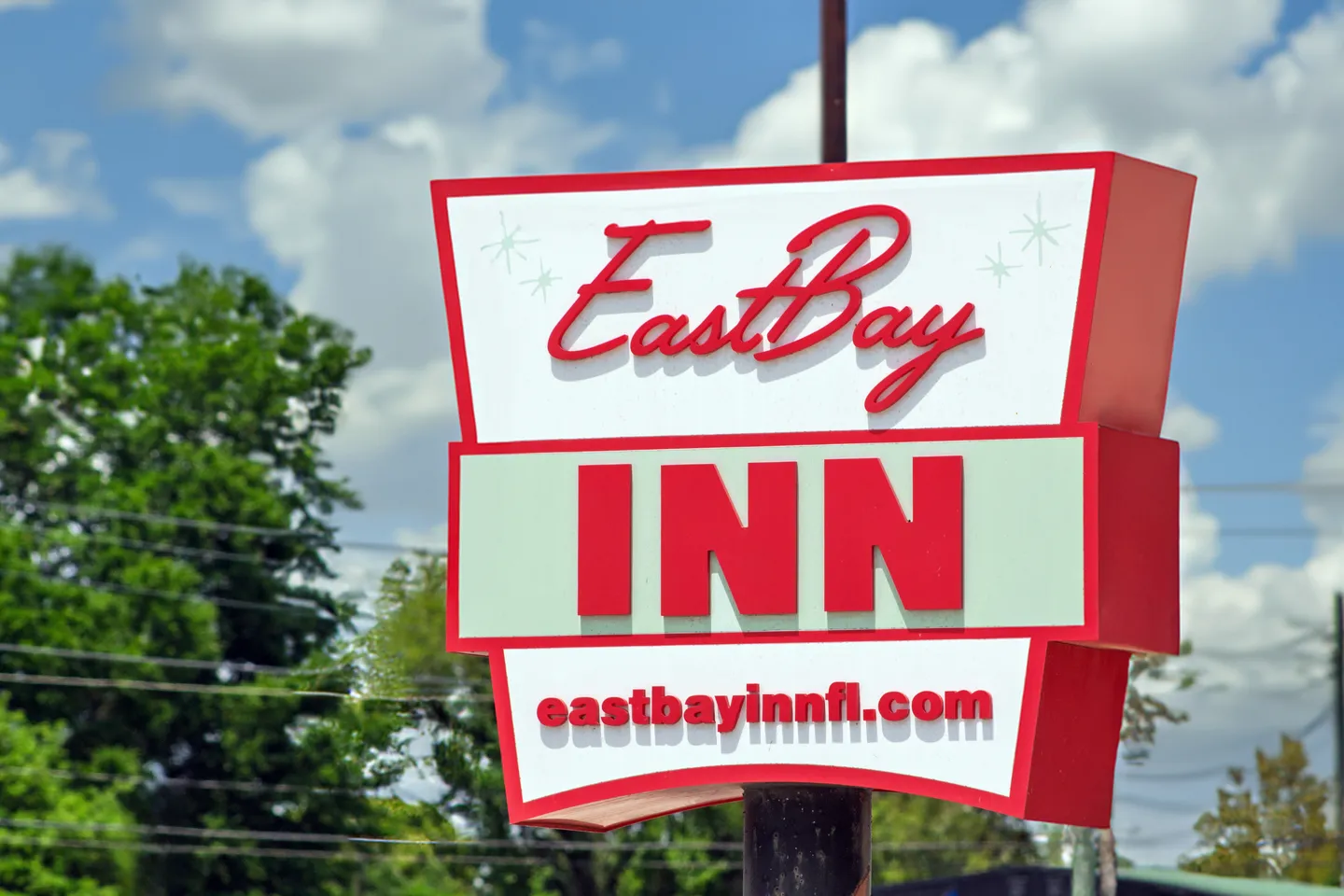 Outdoor signage for East Bay Inn with a red and white retro design under a partly cloudy sky.