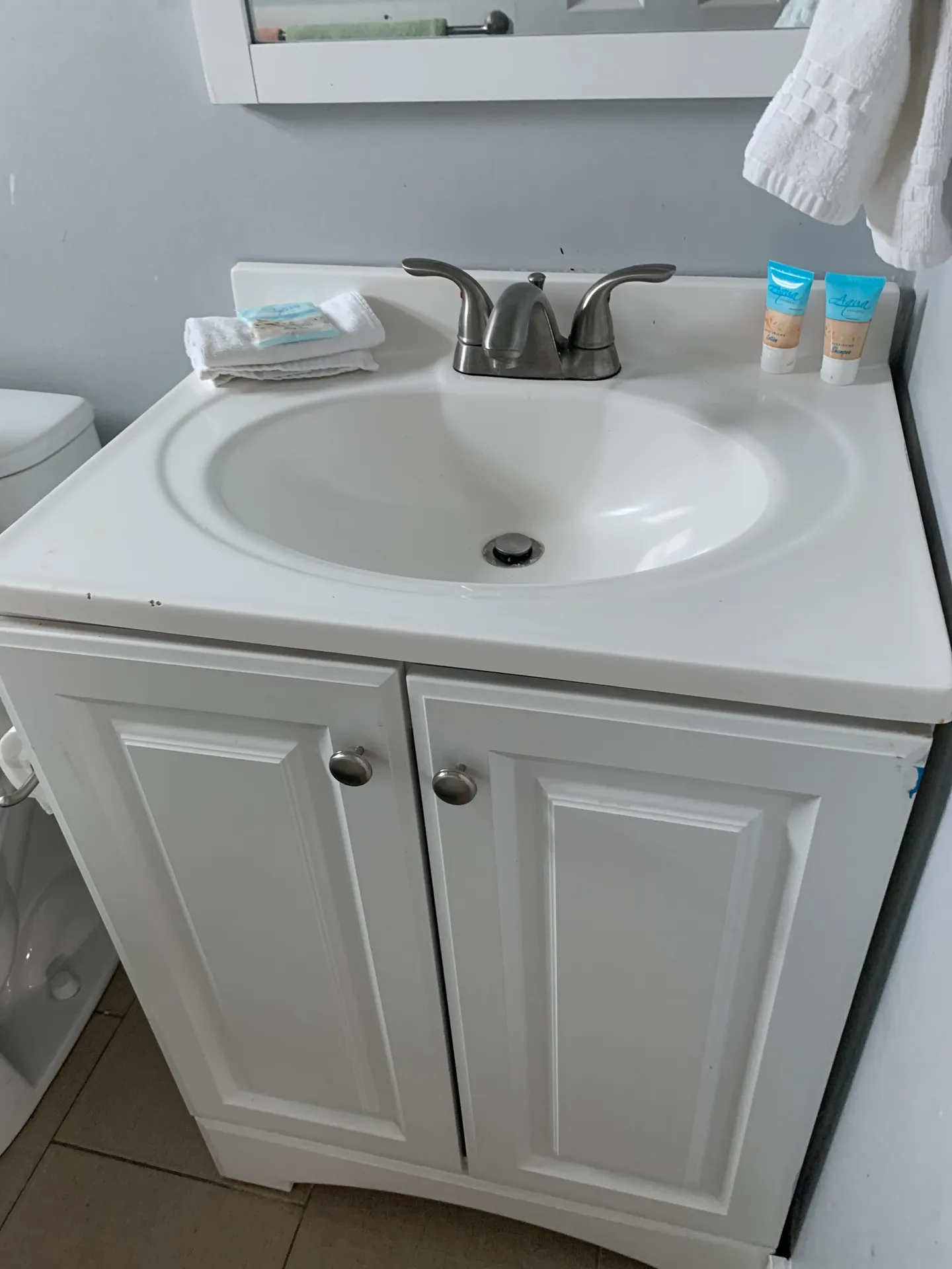 Bathroom vanity with a white countertop, oval sink, brushed metal faucet, and two white cabinet doors.