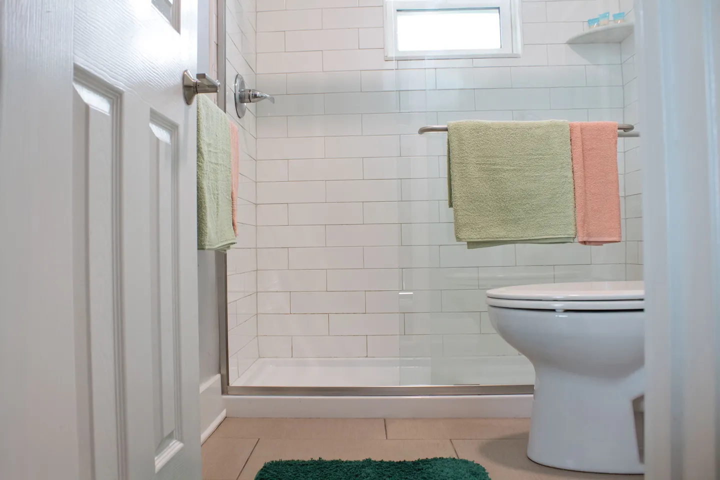 Bathroom with white subway-tiled walk-in shower, glass sliding door, toilet, and folded towels.