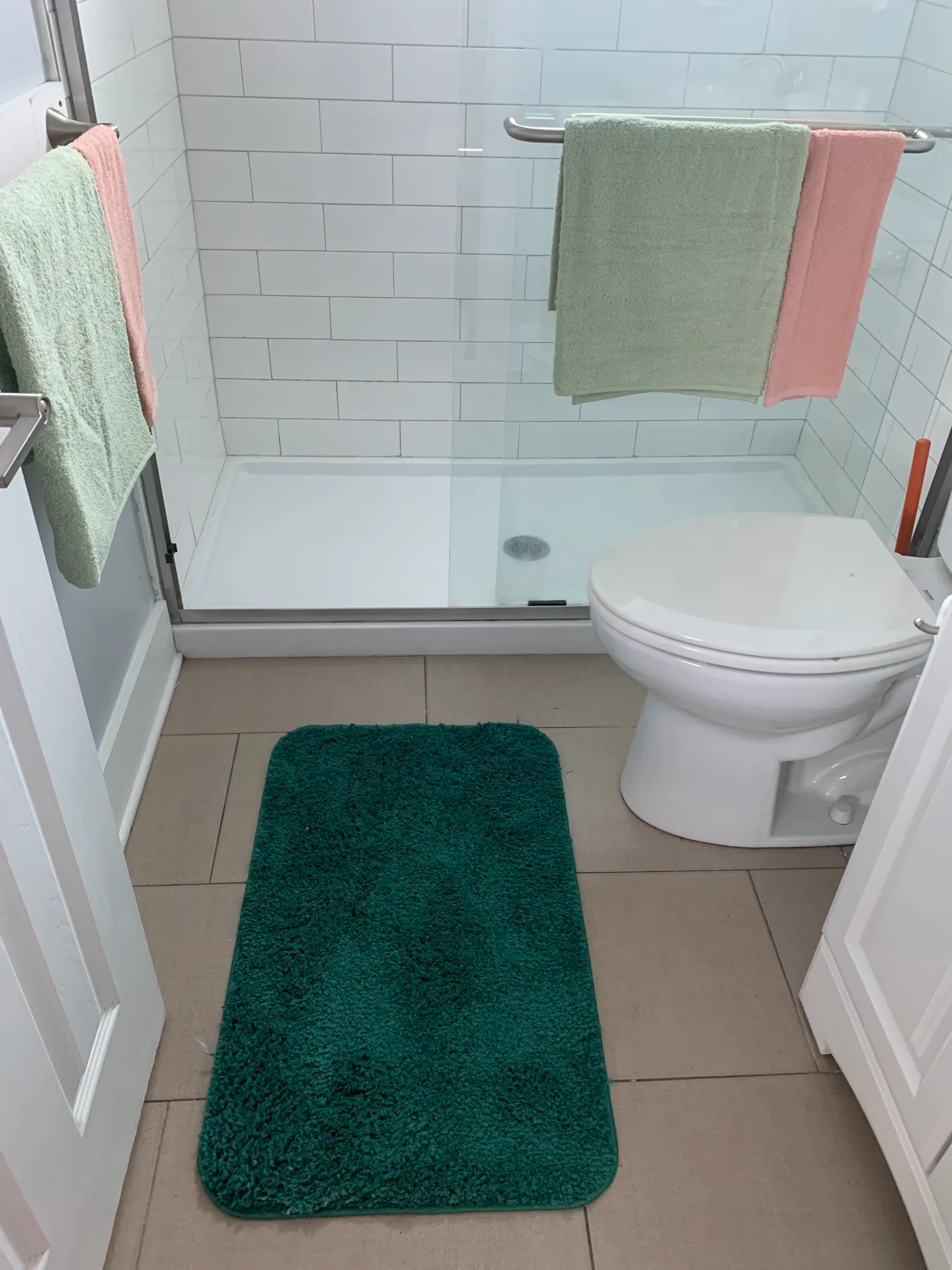 Bathroom showing a walk-in shower with white subway tile, sliding glass doors, a toilet, and a teal bath rug.