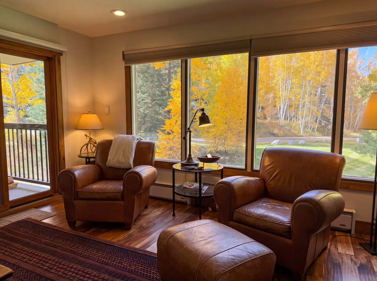 Seating area with two leather armchairs, an ottoman, and large windows overlooking autumn foliage.