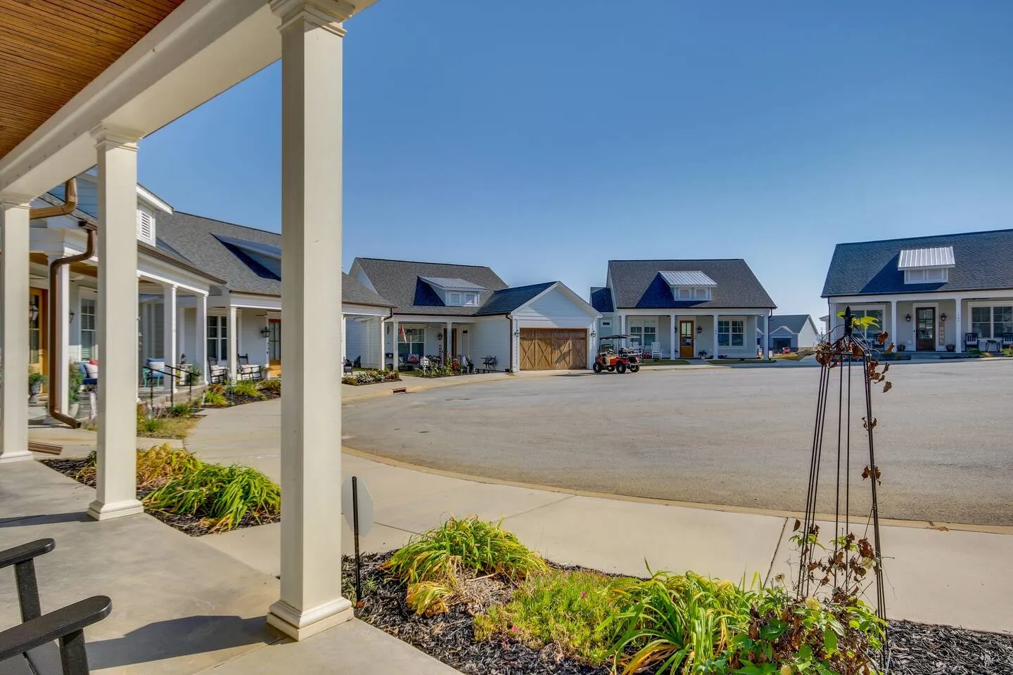 View from a covered front porch looking out across a cul-de-sac of modern cottage-style homes under a clear blue sky.