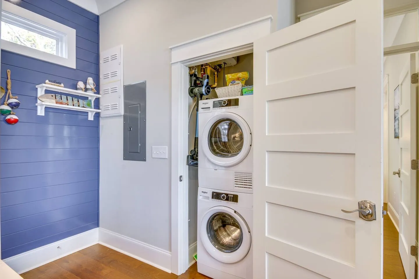 Open closet revealing a stacked white washer and dryer next to a blue shiplap accent wall.