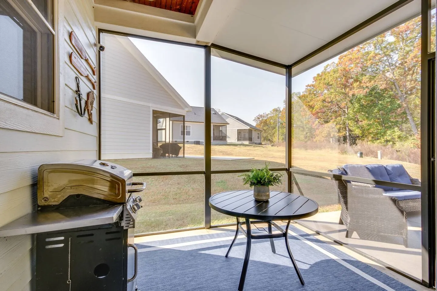 Screened-in porch featuring a barbecue grill, small round table with a potted plant, and a view of the adjacent yard and houses.