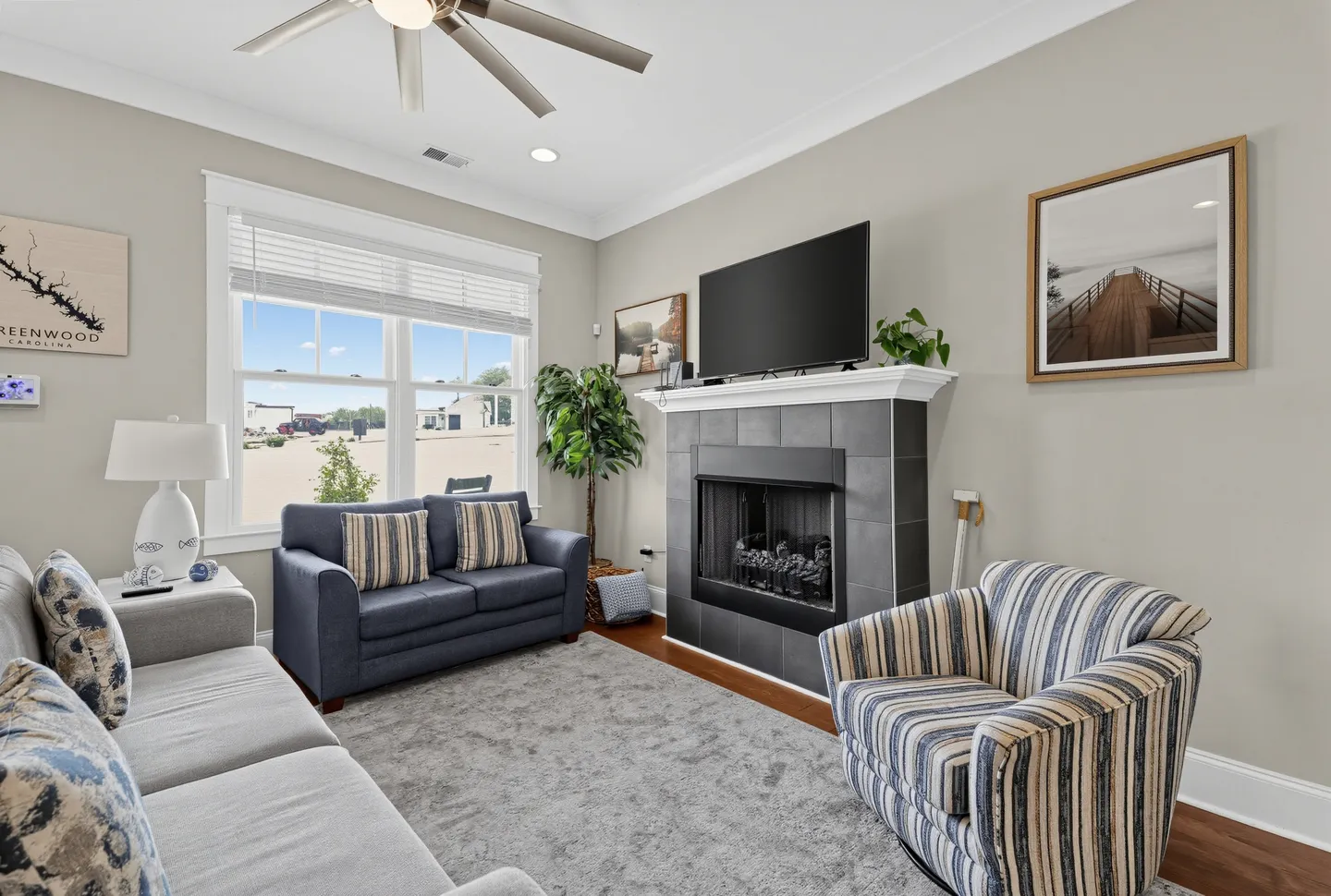 Living room with a tiled fireplace, mounted flat-screen TV, blue love seat, striped armchair, and neutral sofa around a grey rug.