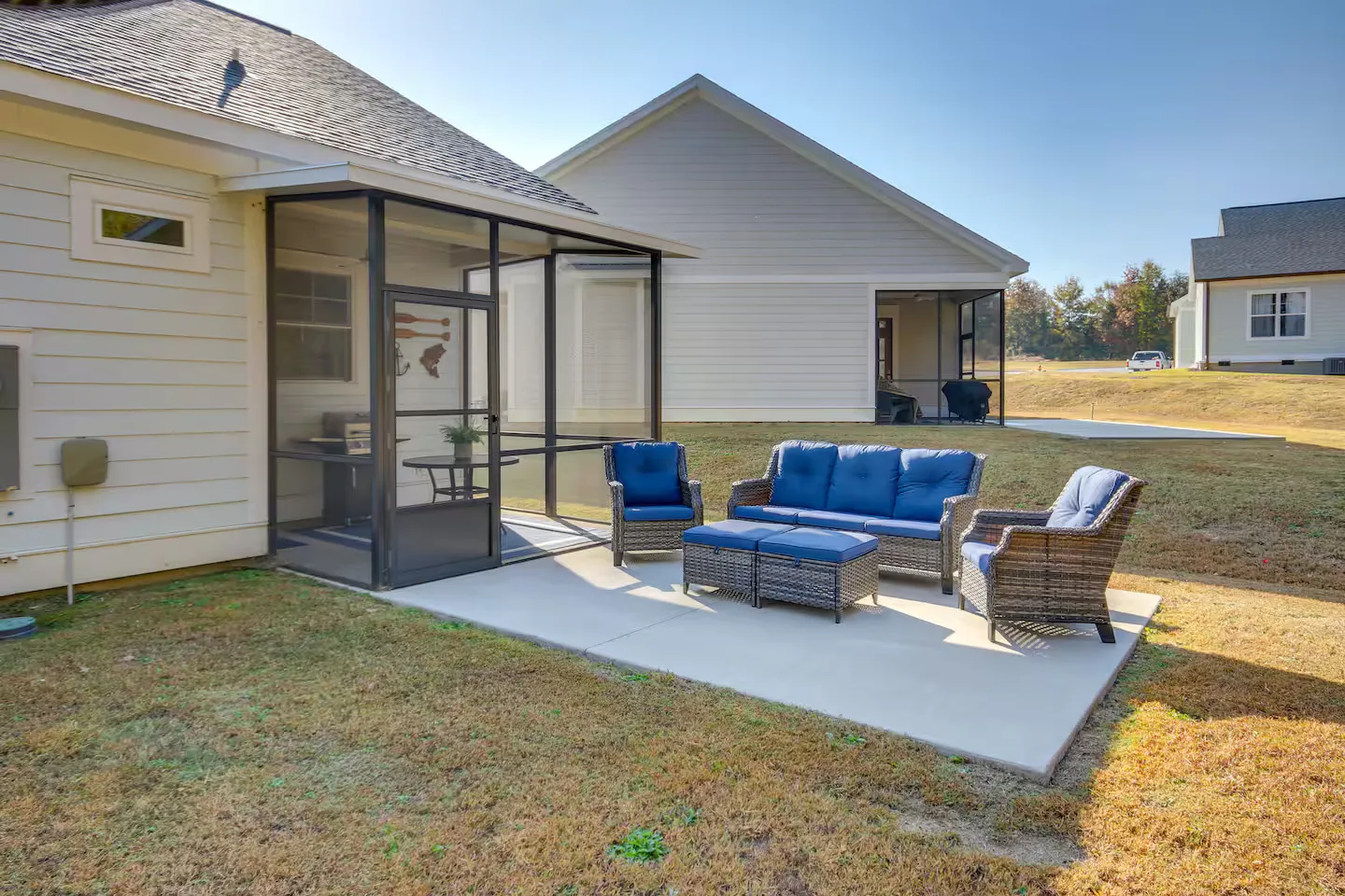 Concrete patio with blue cushioned outdoor seating next to a screened-in porch on the exterior of a home.