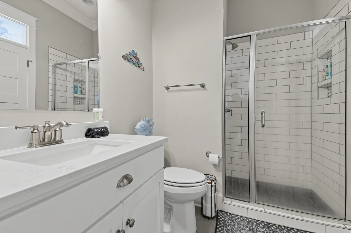 Bathroom featuring a white vanity with silver fixtures, a toilet, and a glass-enclosed walk-in shower with white subway tile.