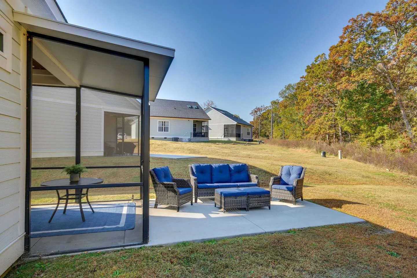 Outdoor patio with blue cushioned wicker furniture next to a screened-in porch overlooking an open grassy yard.