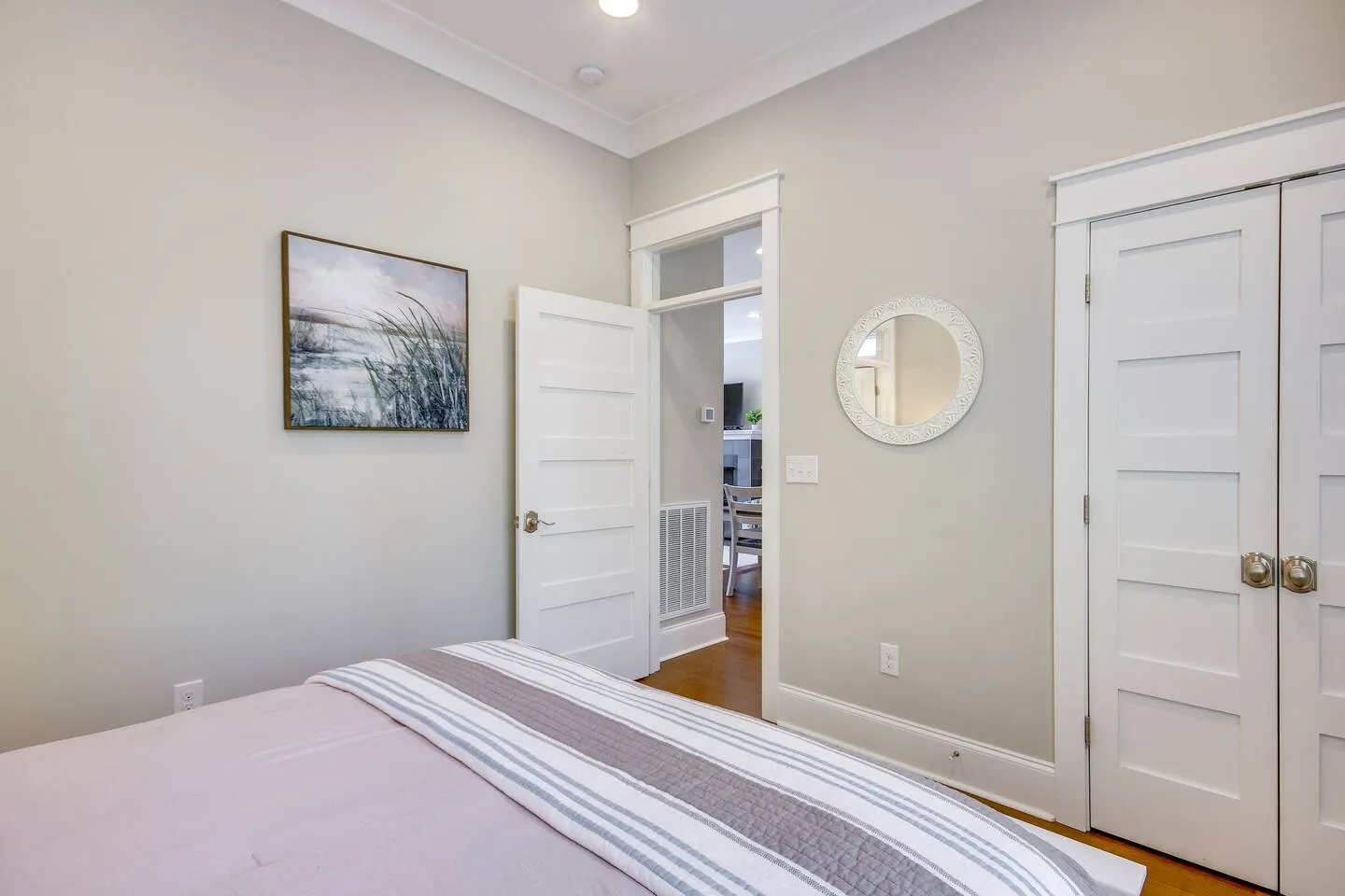 Bedroom with light gray walls, white five-panel interior doors, a round decorative mirror, and the foot of a bed in the foreground.