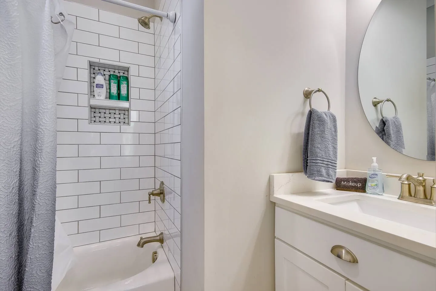 Bathroom showing a subway-tiled shower and tub combination next to a vanity with an undermount sink and round mirror.