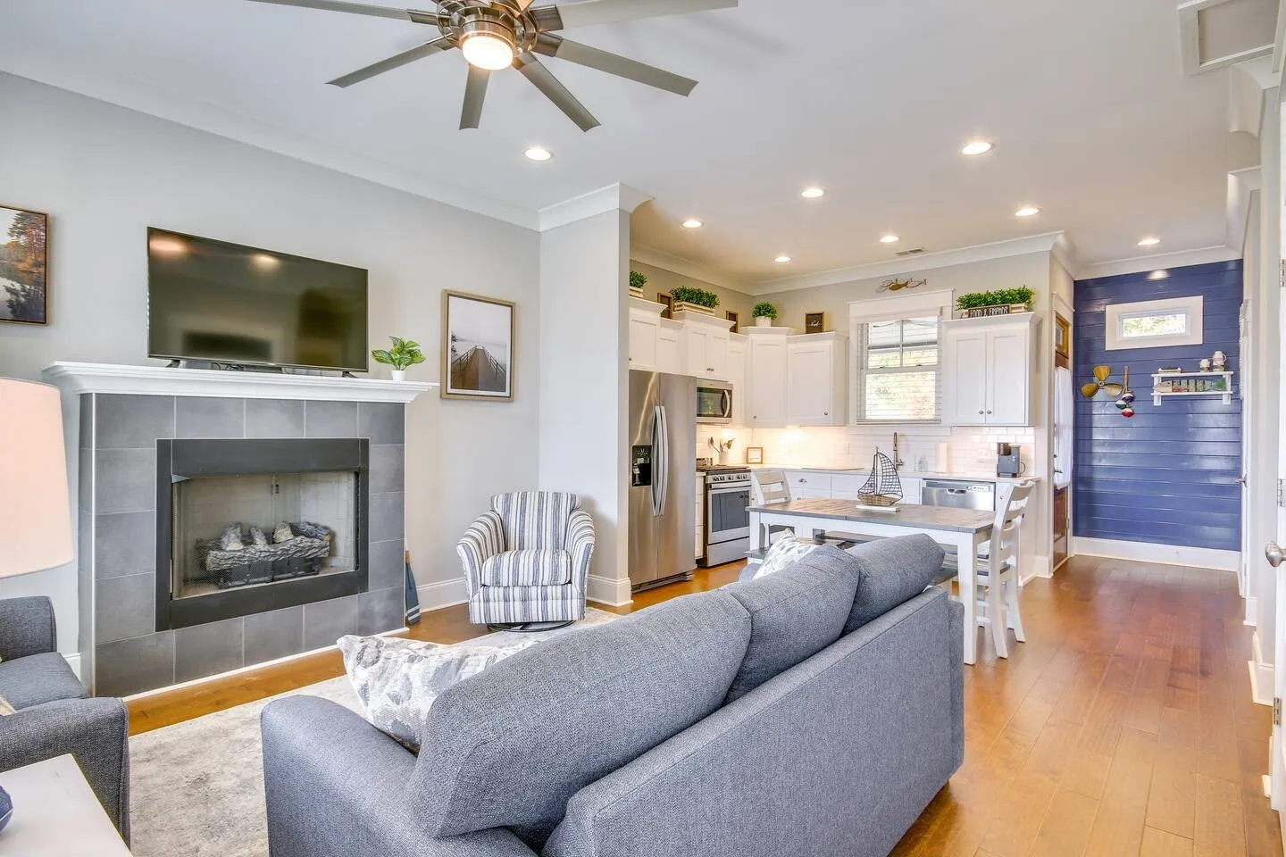 Open-concept living room with gray sofa, fireplace, and mounted TV, extending into the dining area and kitchen.