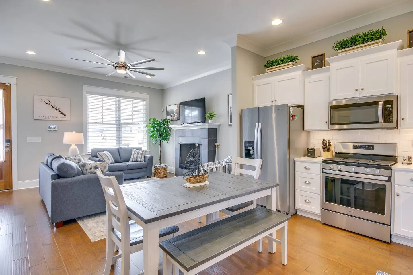 Open-concept interior featuring a dining table with bench seating, adjacent kitchen with stainless steel appliances, and a living room with sofas and a fireplace.