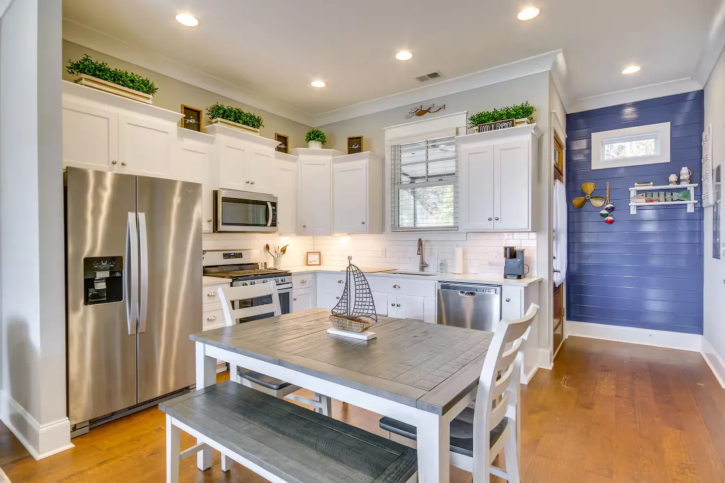 Kitchen and dining area with white cabinetry, stainless steel appliances, a wooden dining table with a bench, and a blue accent wall.