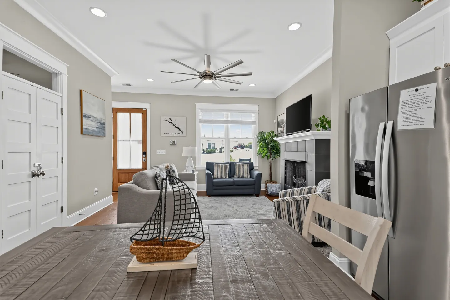 Open-concept living room viewed from a wooden dining table, featuring a fireplace, mounted TV, sofas, and an entrance door.