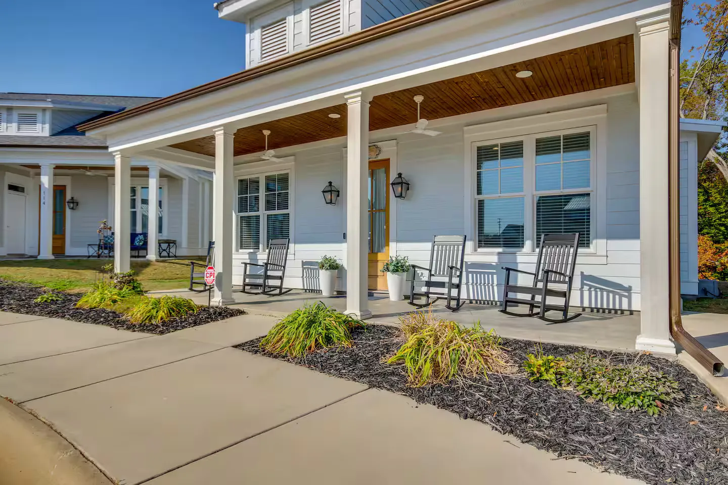 Front porch of a white siding home with white columns, wood-paneled ceiling, and black rocking chairs.
