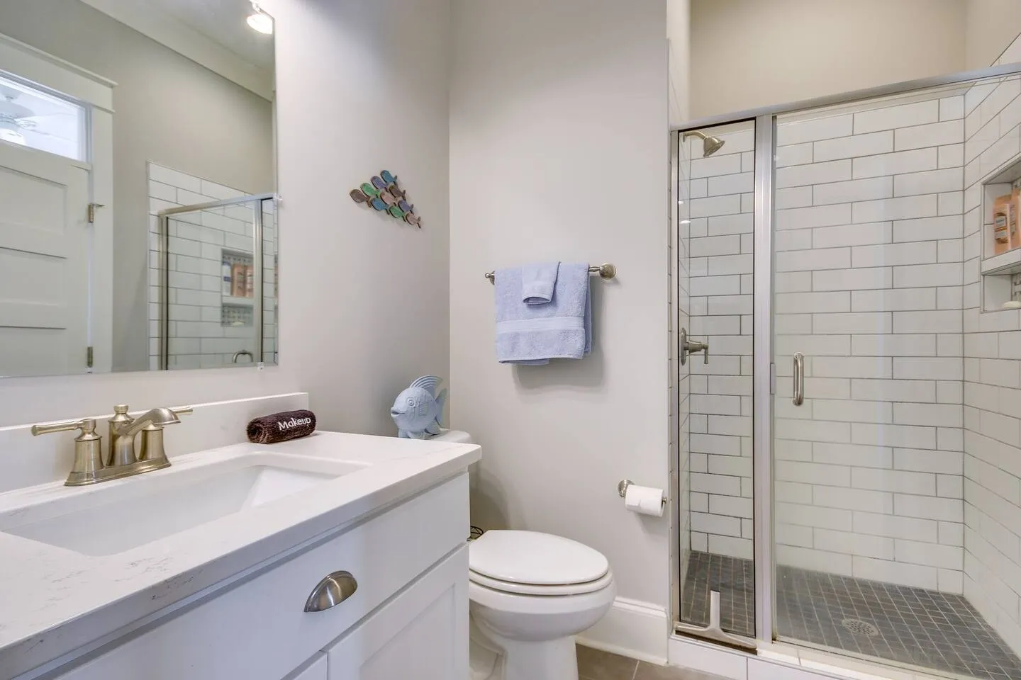 Bathroom with white vanity, toilet, and glass-enclosed walk-in shower with white subway tile.