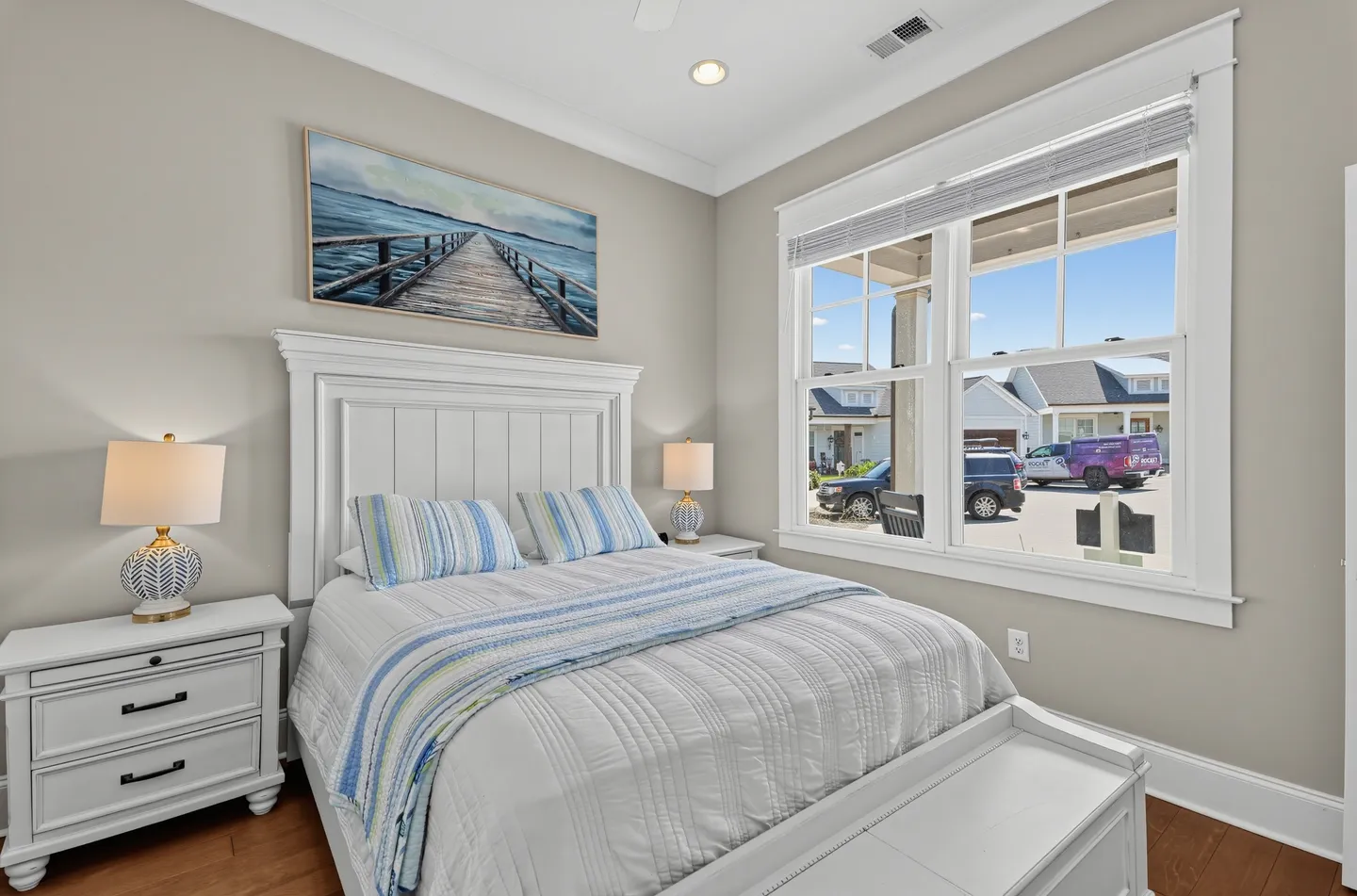 Bedroom with a white panel bed, striped pillows, matching white nightstands with lamps, and a large window.