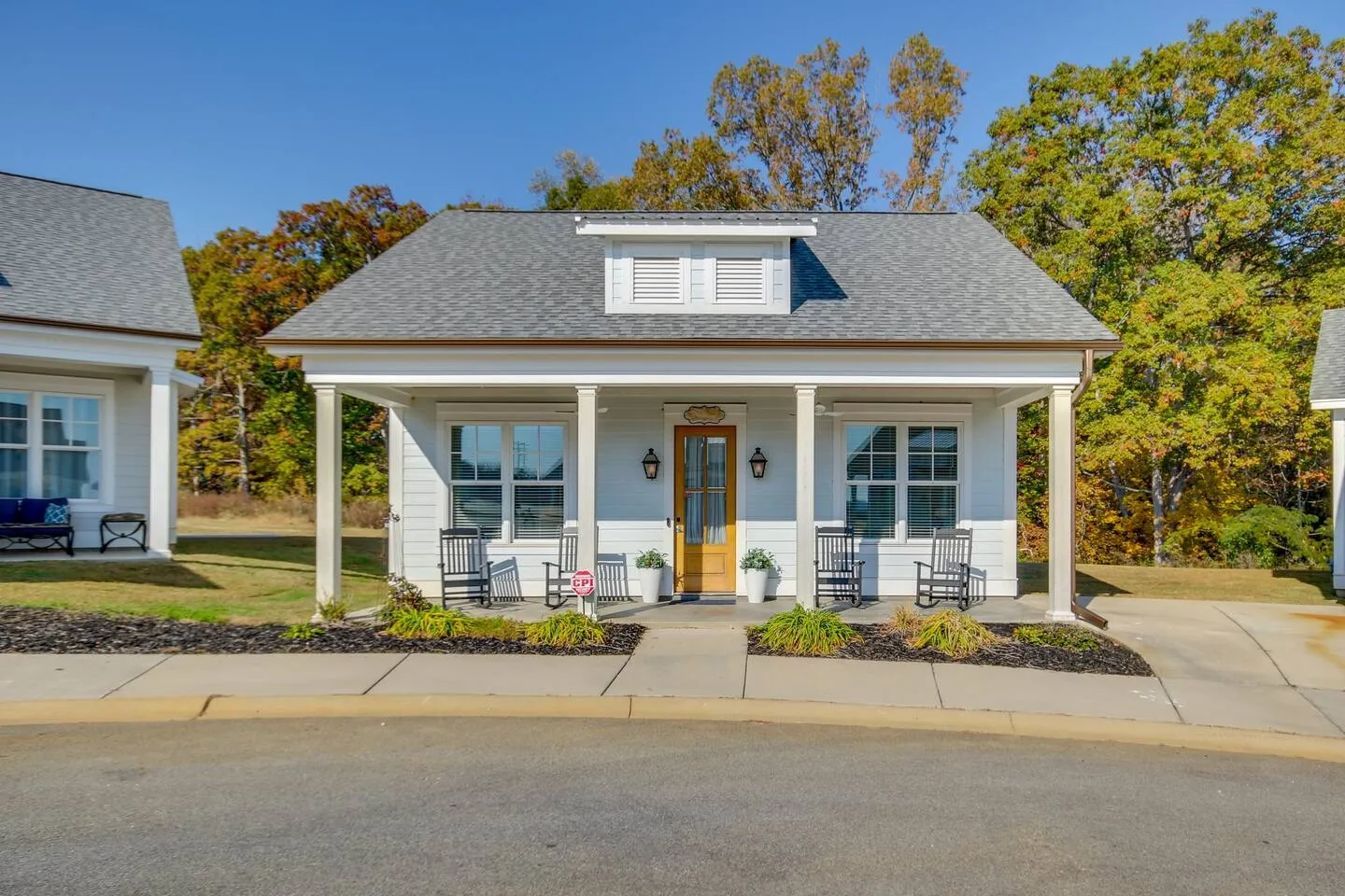 Exterior view of a small white cottage with a covered front porch featuring rocking chairs.