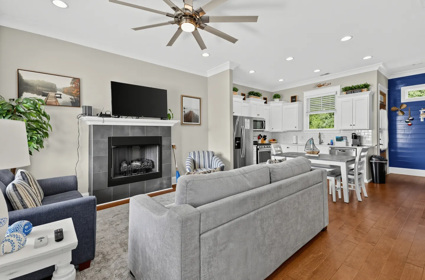 Open-concept living room and kitchen featuring a tiled fireplace with a mounted TV, a grey sofa, and white kitchen cabinets.