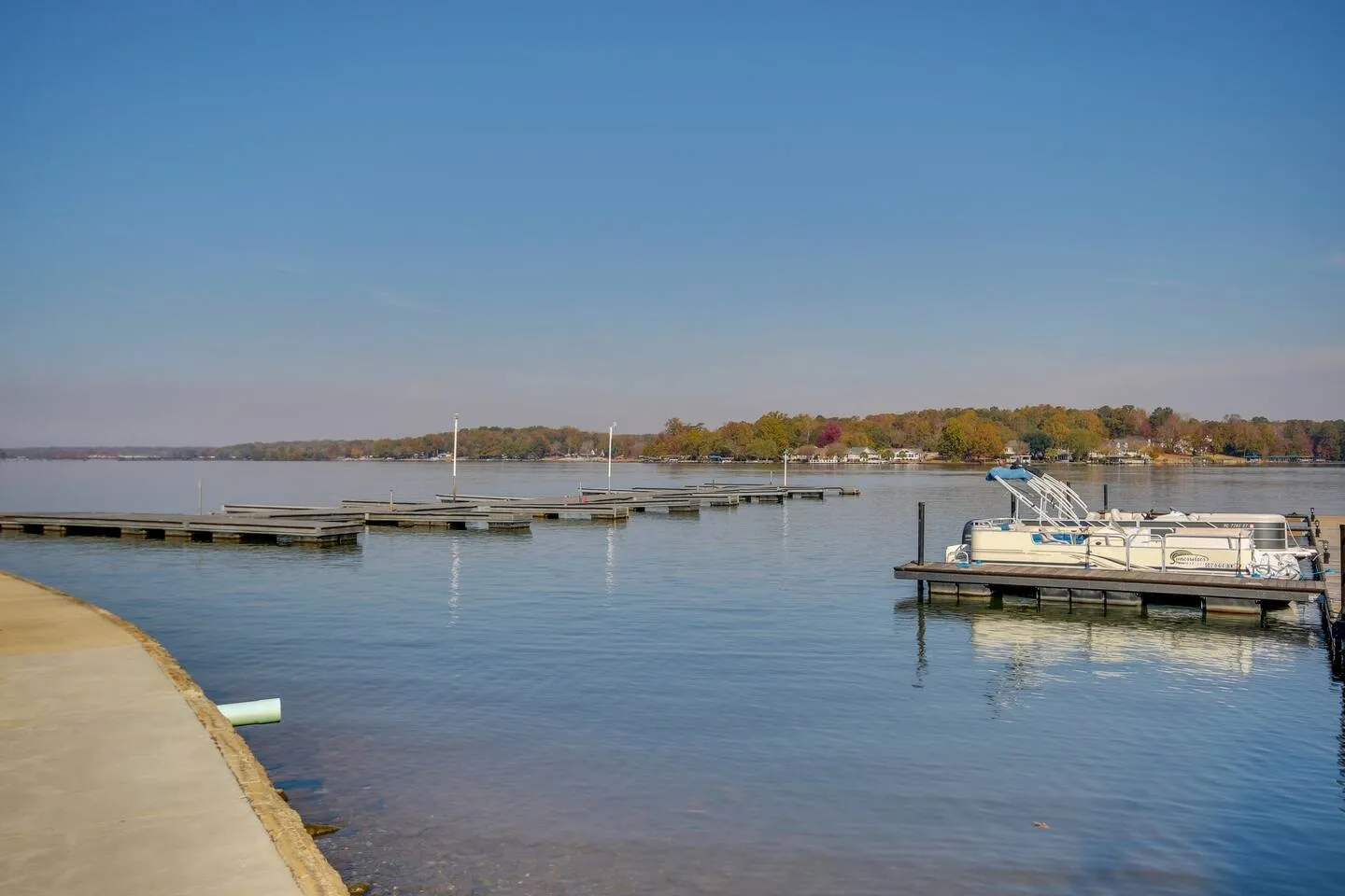 A wide view of a calm lake with boat slips and a pontoon boat docked on a clear day.