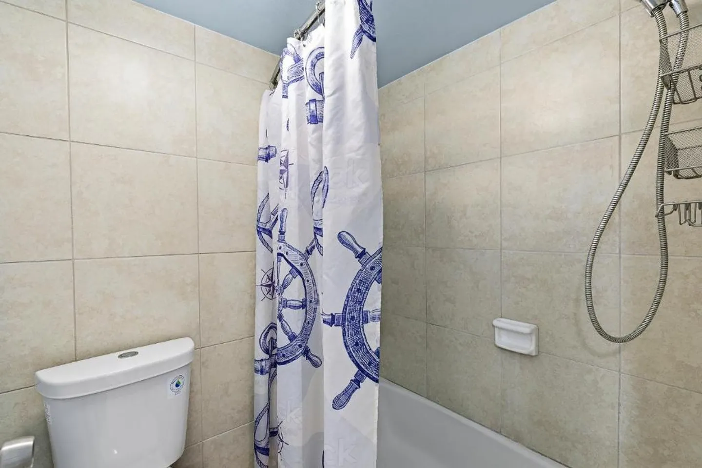 Bathroom showing a tiled tub and shower enclosure with a nautical-patterned shower curtain next to a white toilet.