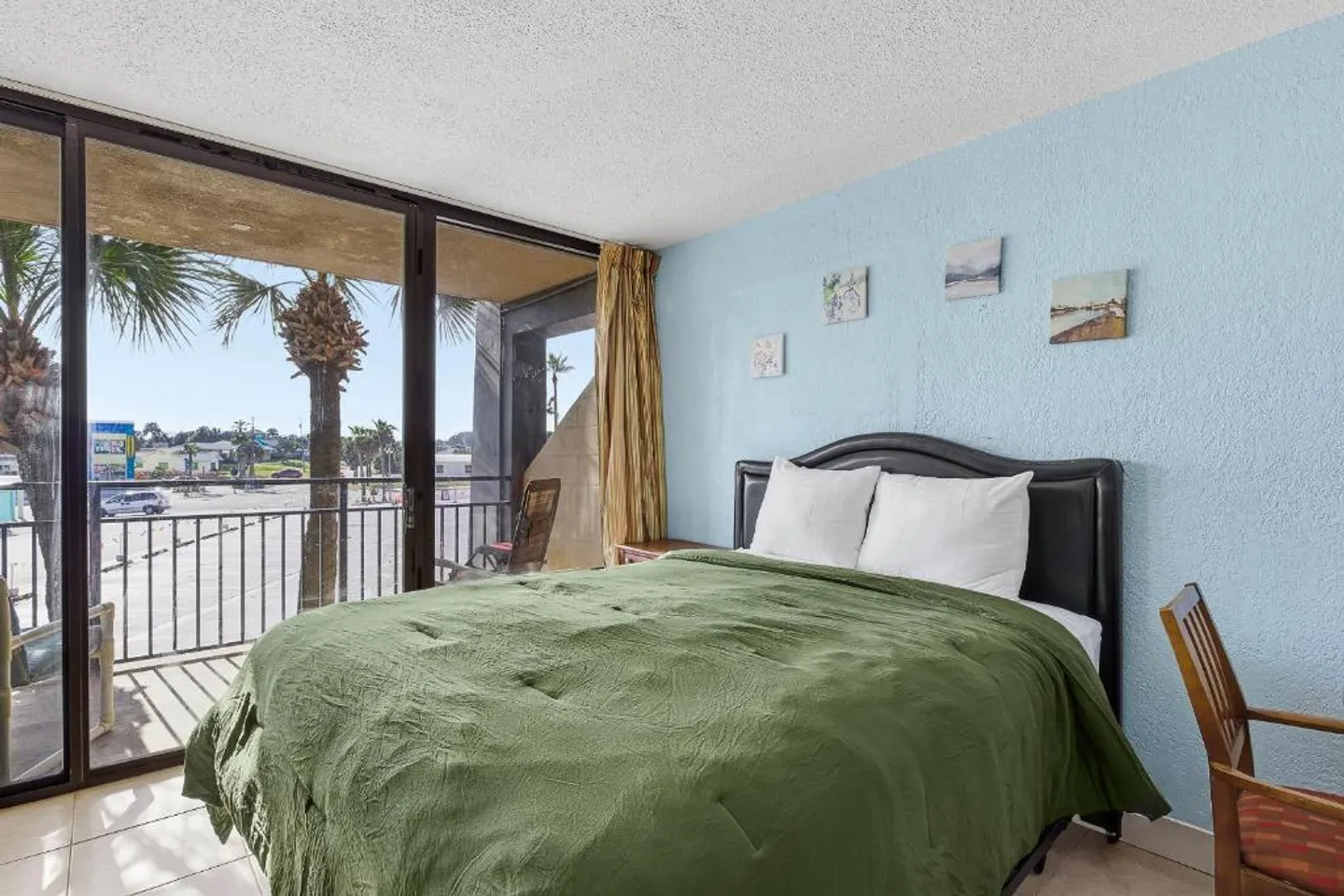 Bedroom with a bed made with an olive green comforter next to sliding glass doors that open to a balcony.