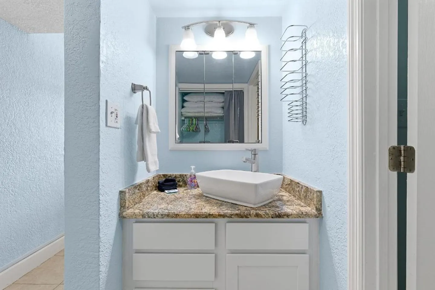 Bathroom vanity nook with light blue textured walls, granite countertop, rectangular vessel sink, medicine cabinet mirror, and overhead lighting.