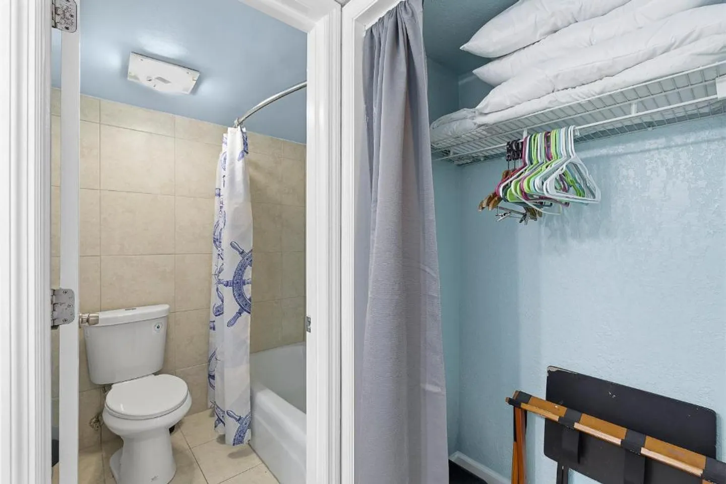 Open doorway showing an adjacent bathroom with a toilet and shower next to a closet with hangers and pillows.