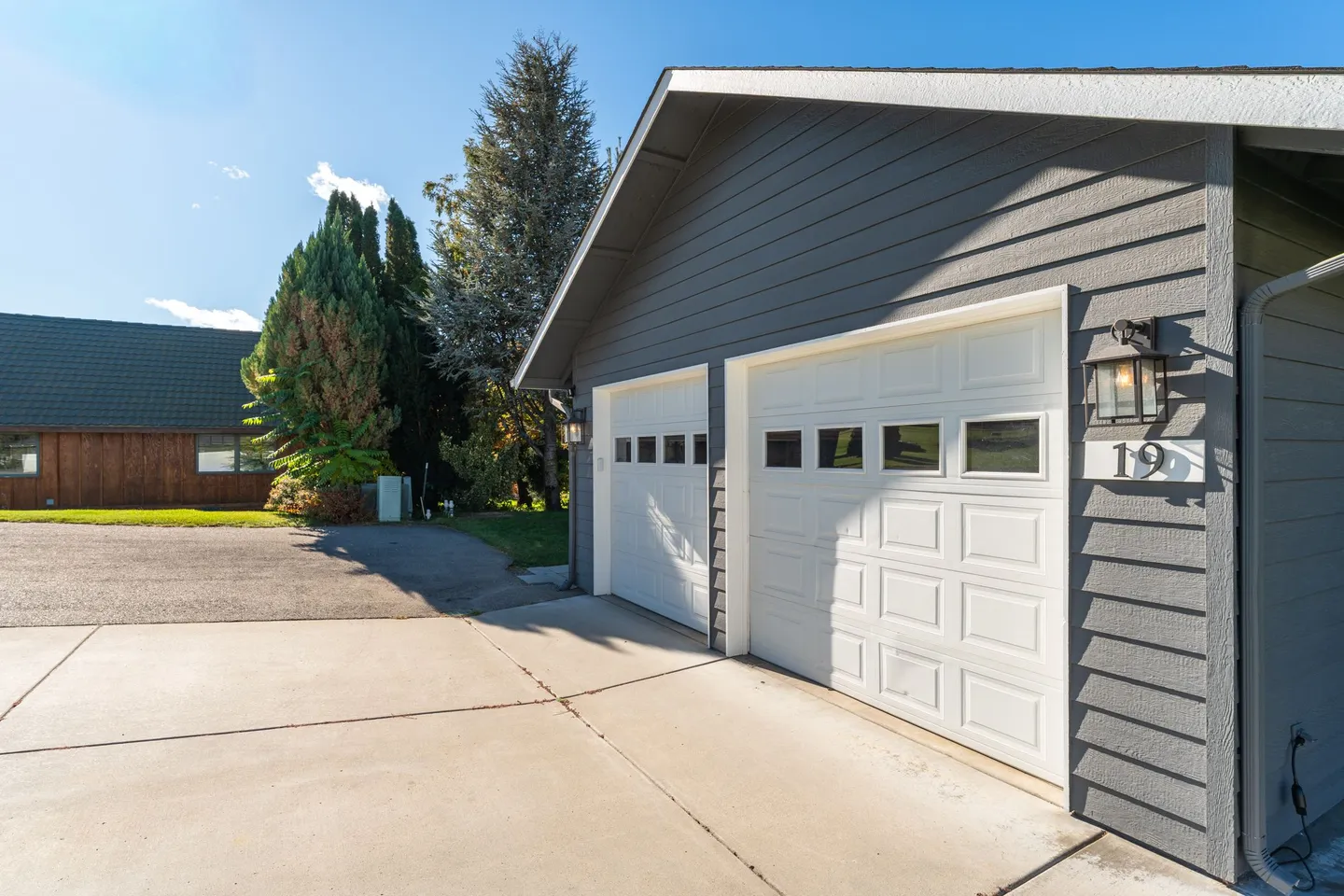 Exterior view of a gray siding garage with two white paneled garage doors and a concrete driveway on a sunny day.
