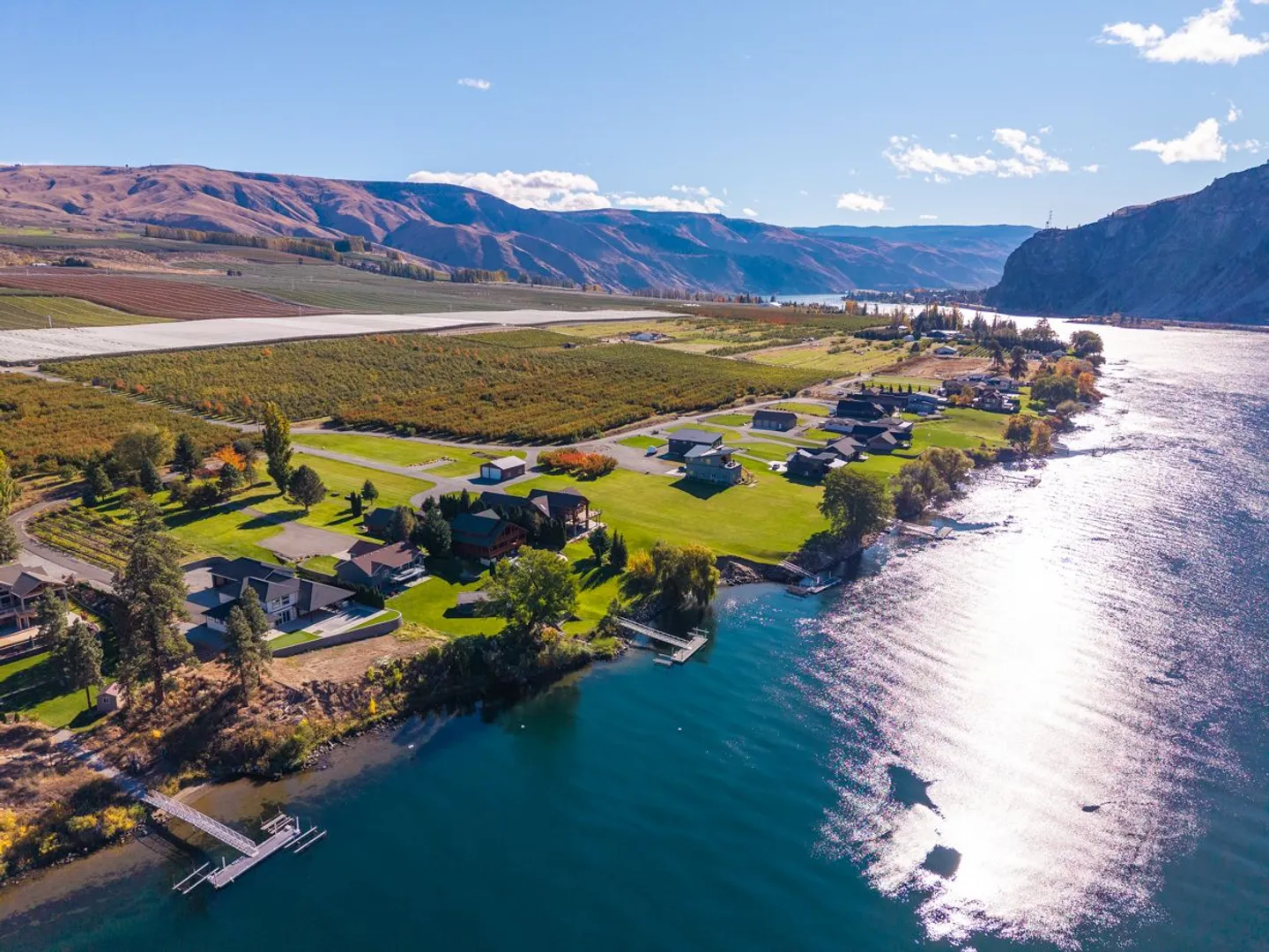 Aerial view of a waterfront community along a wide river with private docks and rolling hills in the background.