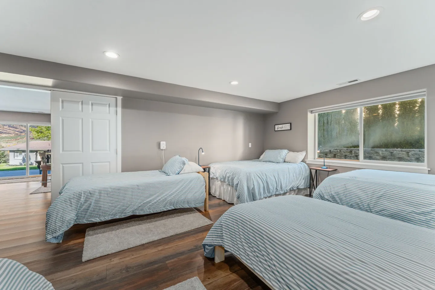 Bedroom with multiple beds dressed in striped bedding, wood-look flooring, and a window.