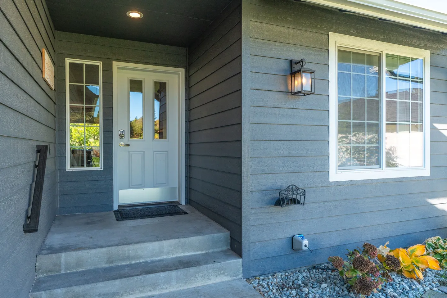 Exterior covered front entry of a house with slate-blue siding, concrete steps, and a white front door.