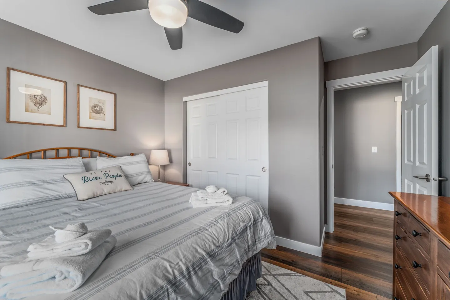 Bedroom featuring a made bed with striped bedding, a wooden headboard, a ceiling fan, a dresser, and a closet with sliding white doors.
