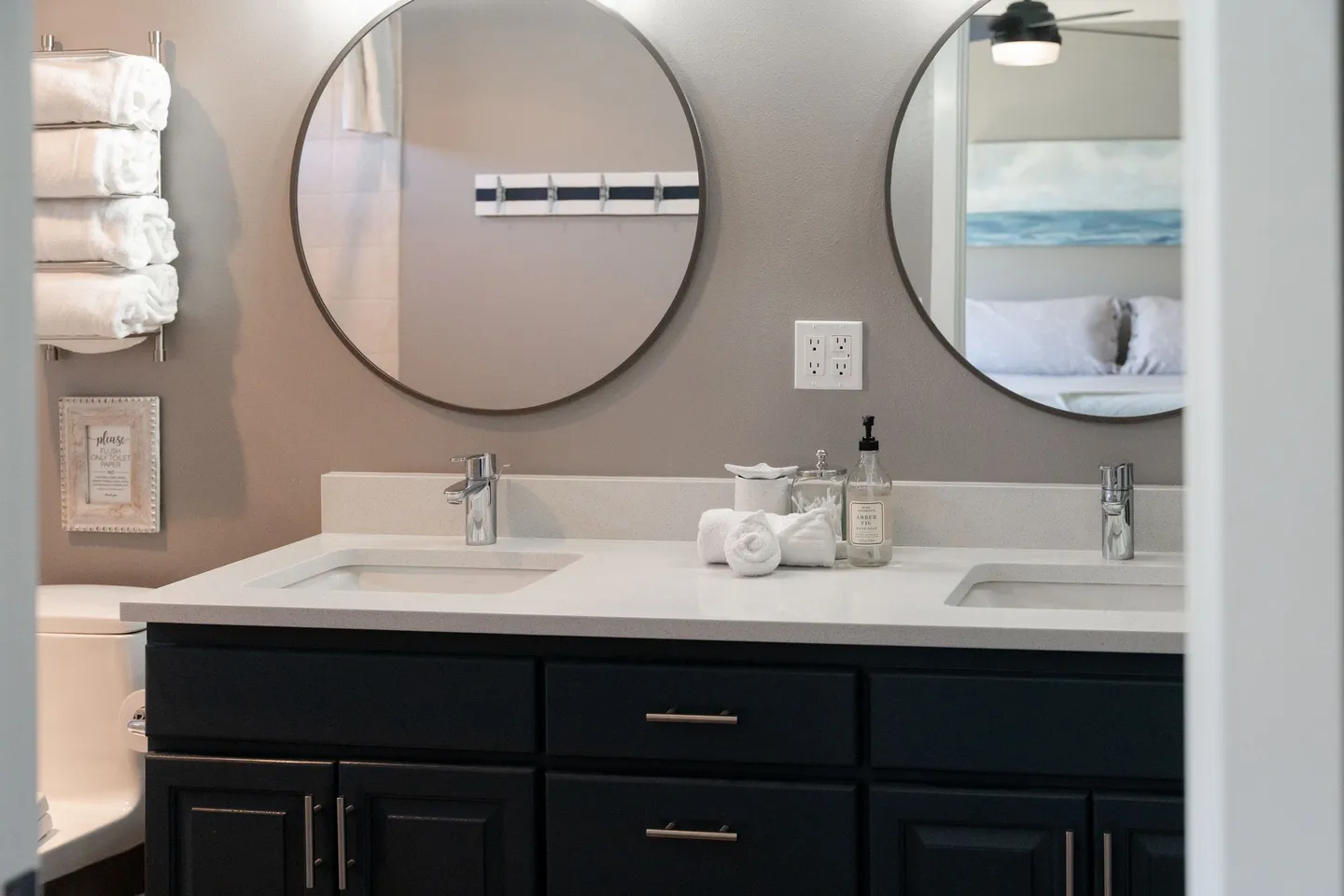 Bathroom double vanity with dark cabinets, two round mirrors, and rolled white towels.