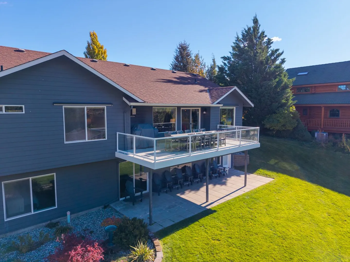 Exterior of a two-story blue house featuring an upper deck with an outdoor dining table and a lower covered patio with seating.