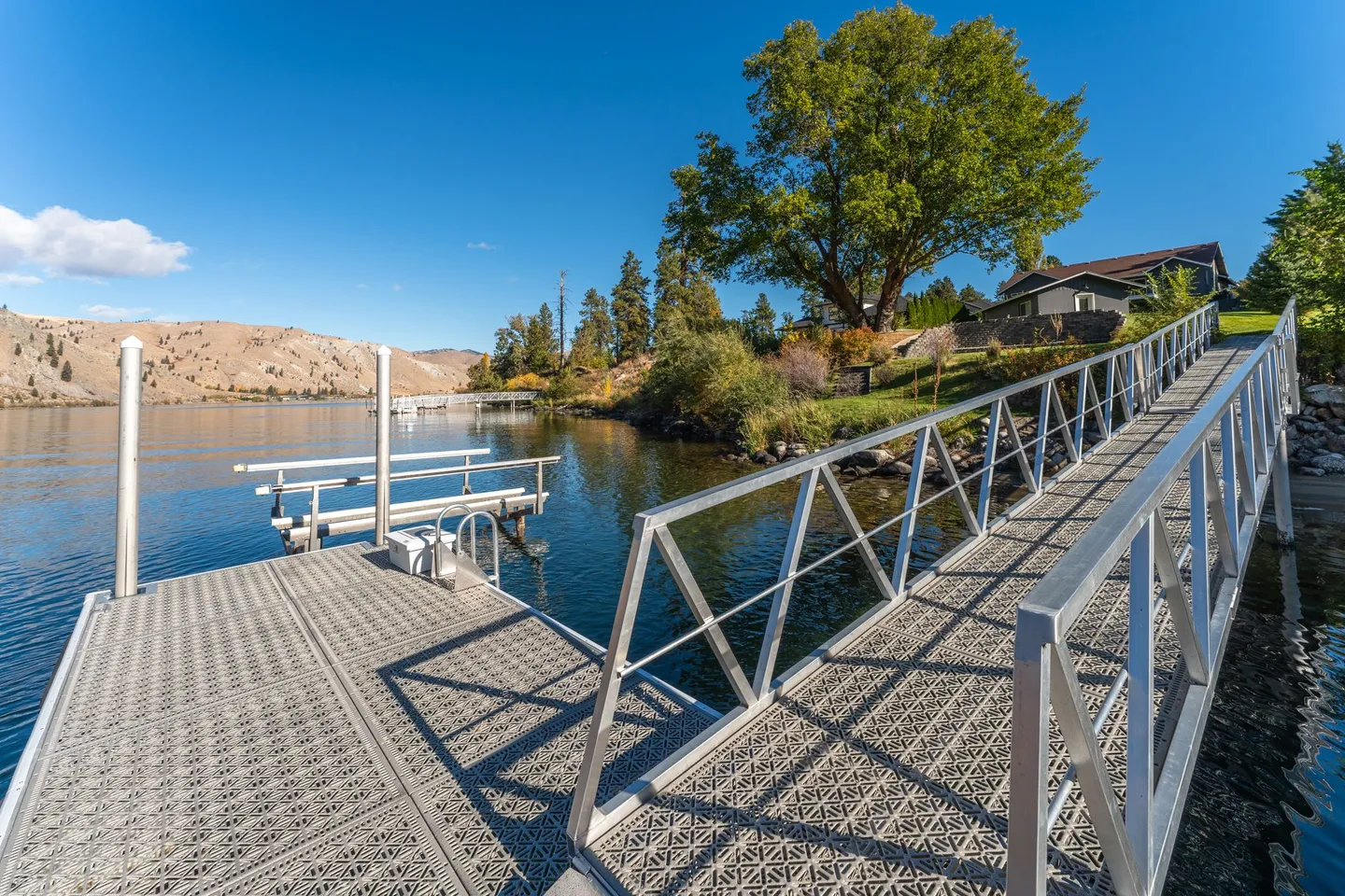 A metal ramp leads down to a private dock with a boat lift on a sunny lake.