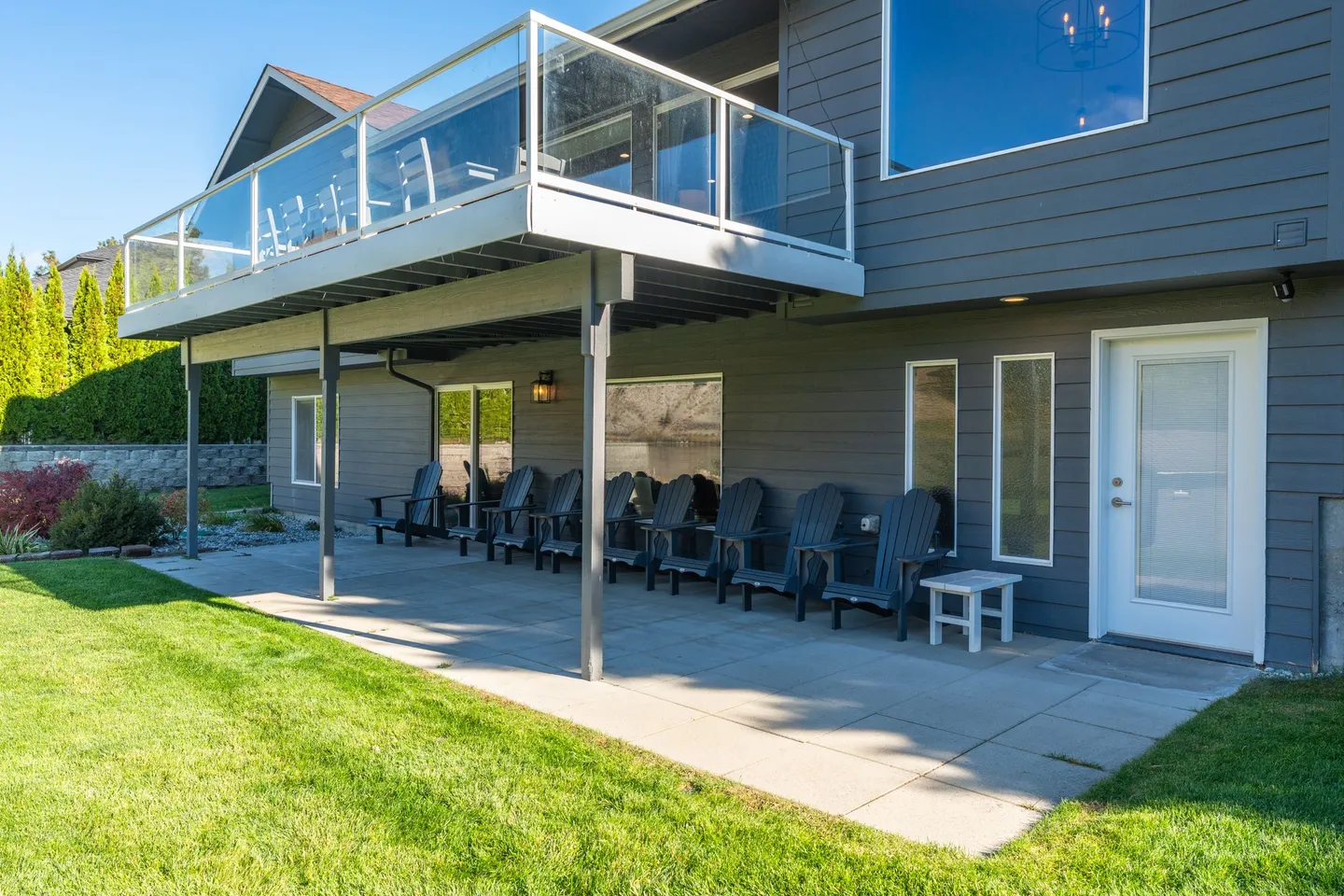 Covered ground-level patio with Adirondack chairs underneath an upper deck with glass railings.