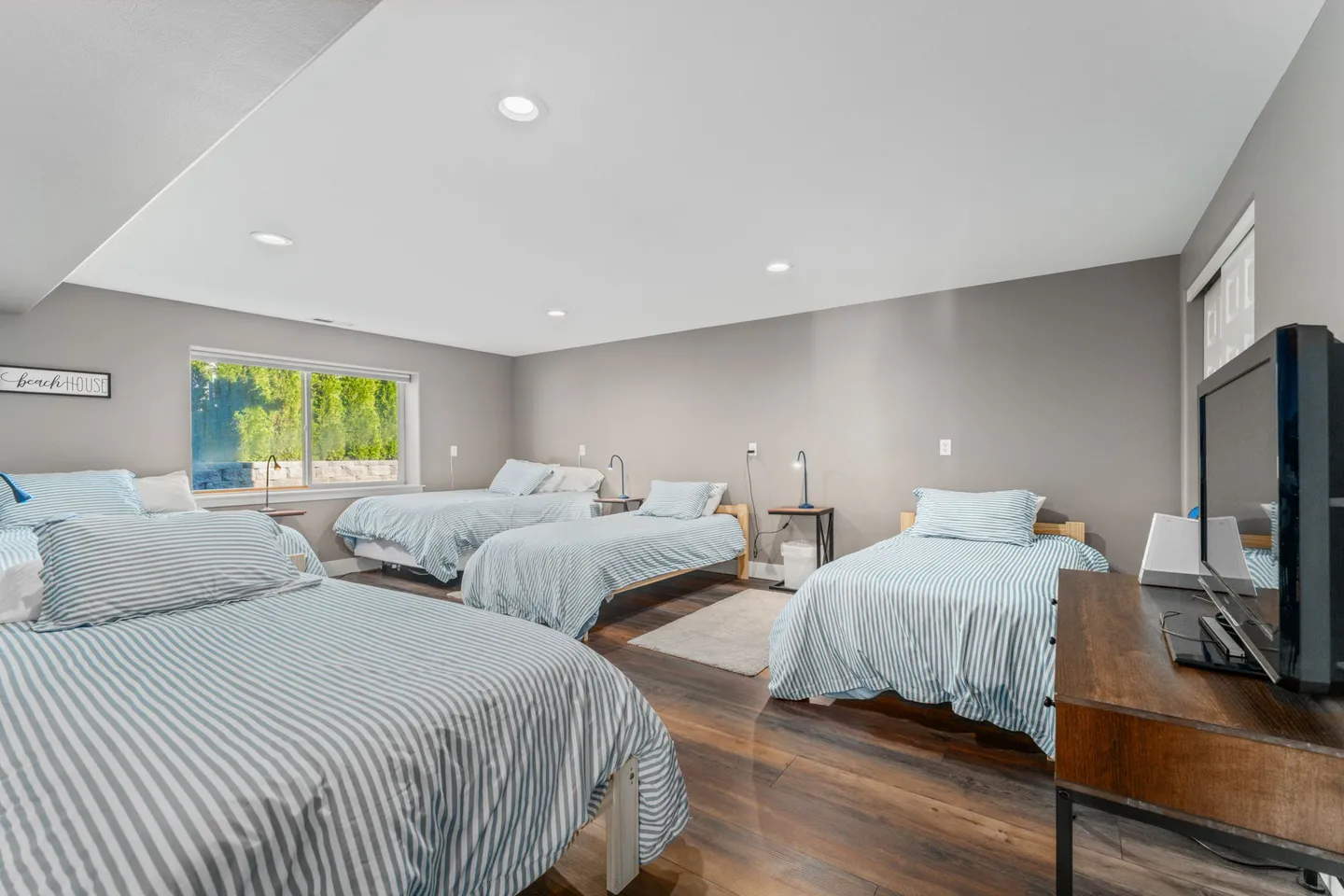 Bedroom with five beds dressed in matching blue and white striped bedding, wood-look flooring, and a flat-screen TV.