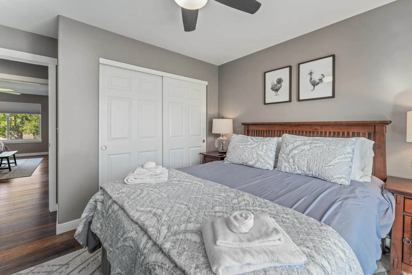 Bedroom with a wooden headboard, light blue patterned bedding, white closet doors, and wood-look flooring.