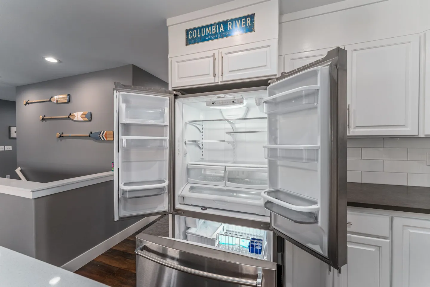 Open stainless steel French-door refrigerator showing empty interior shelves, crisper drawers, and freezer compartment.
