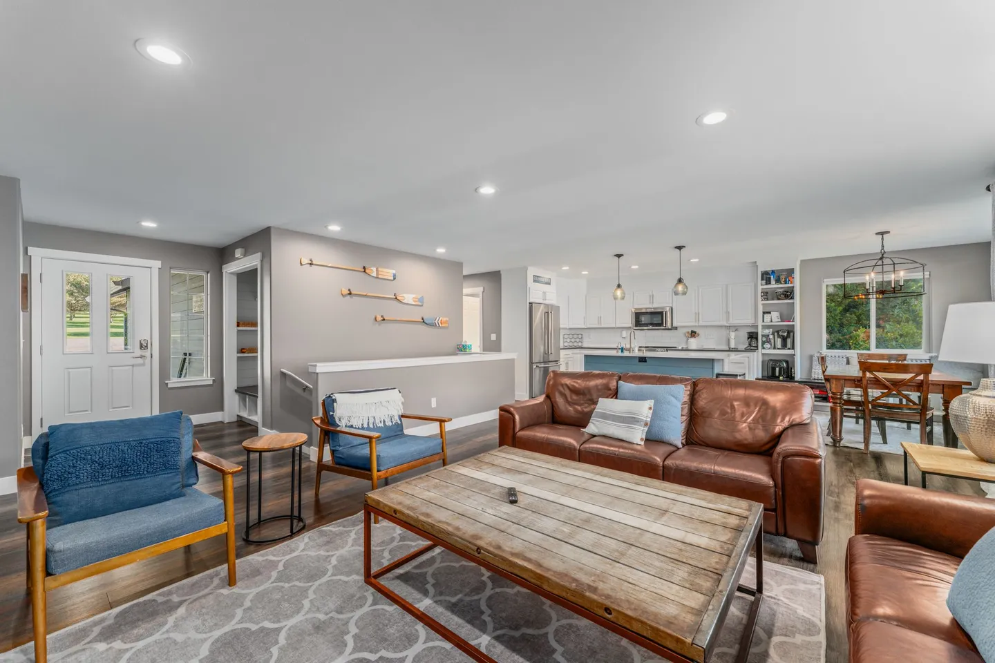 Open-concept living room with leather sofas, blue armchairs, and a view into the kitchen and dining area.