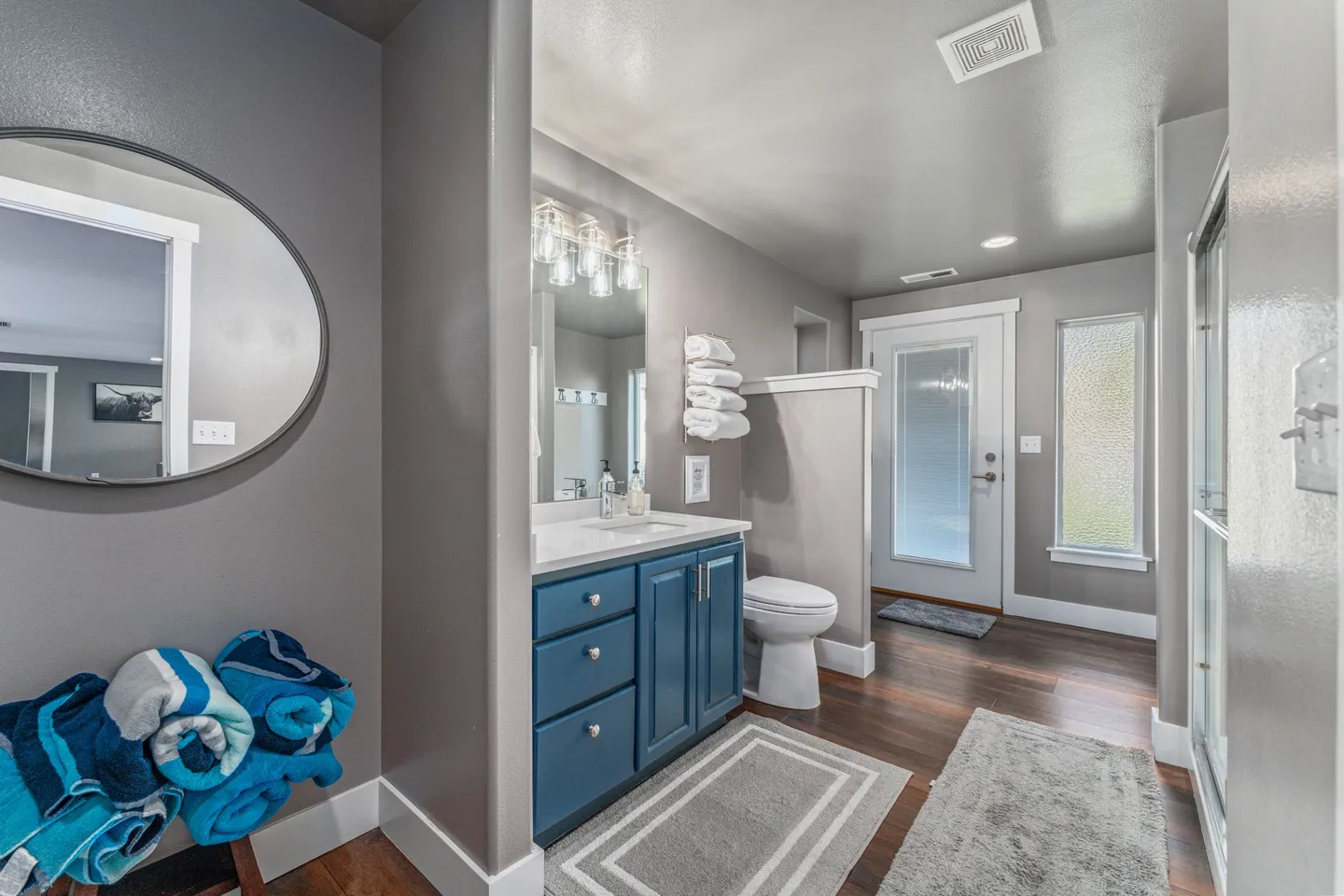 Bathroom featuring a blue vanity with a white countertop, toilet partitioned by a half wall, and a frosted glass door to the exterior.