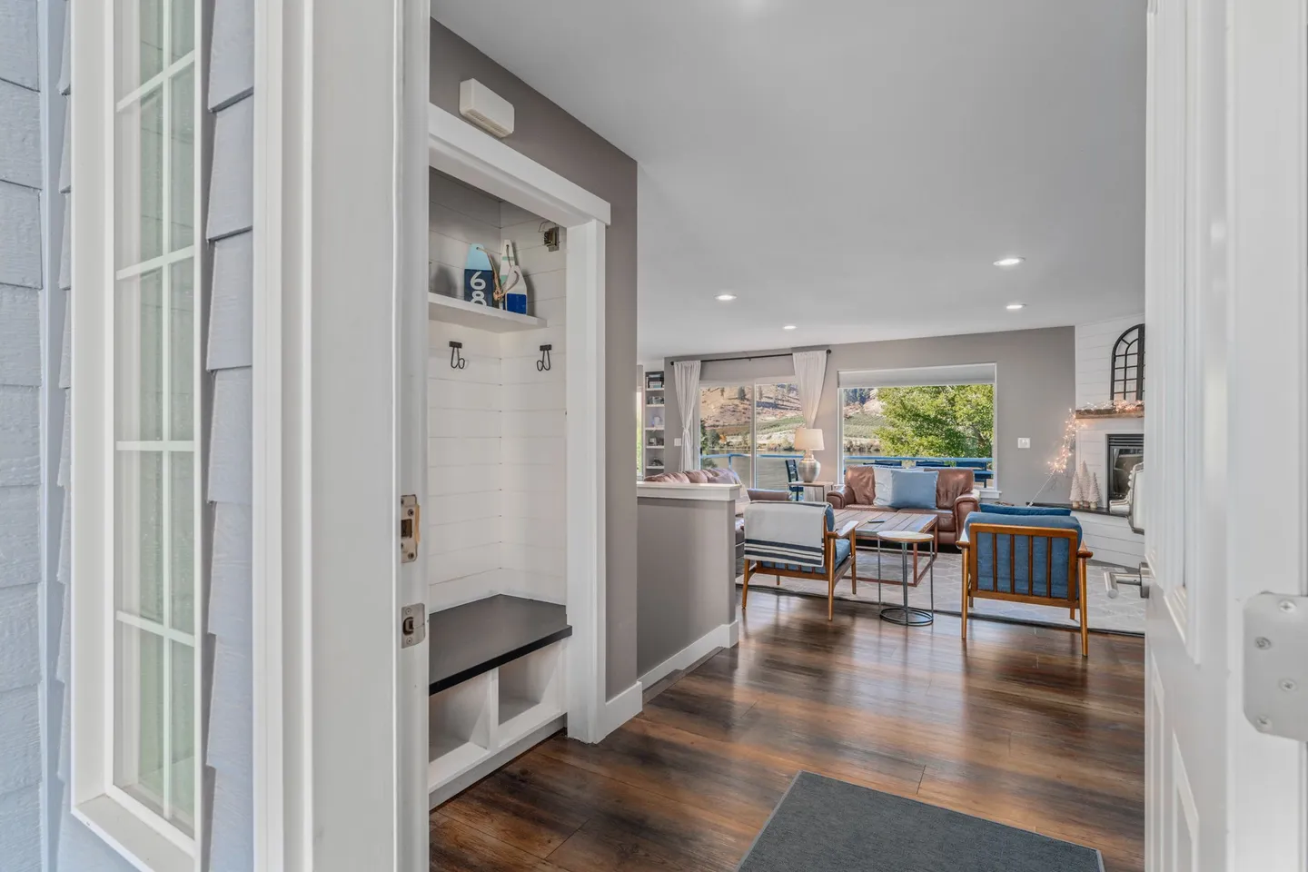 Open doorway view into an entryway with a built-in bench leading into an open living room with scenic window views.