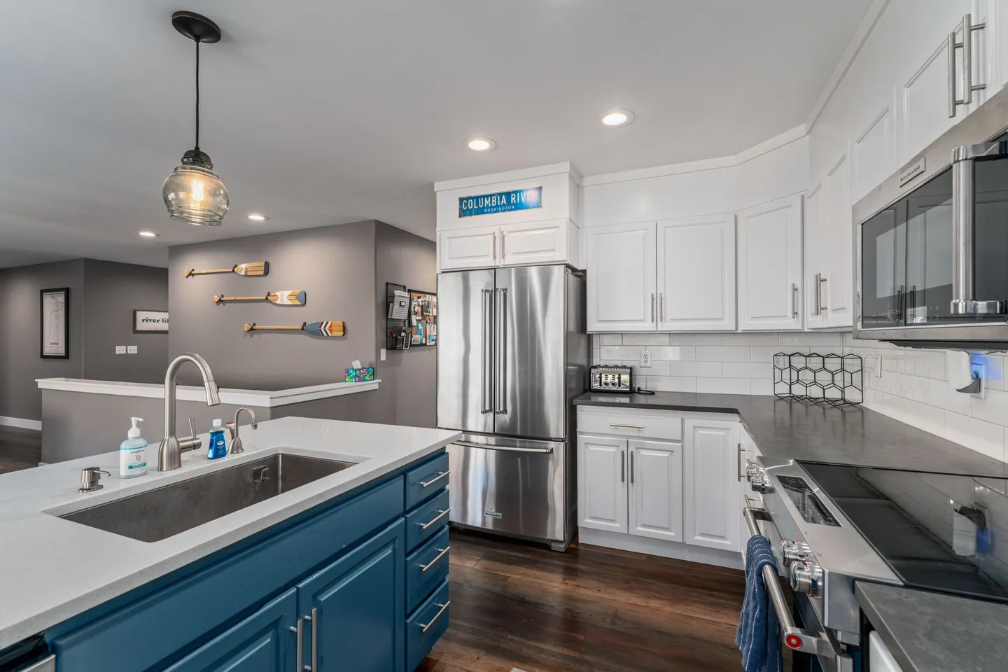 Modern kitchen with stainless steel appliances, dark countertops, white cabinetry, and a blue island.