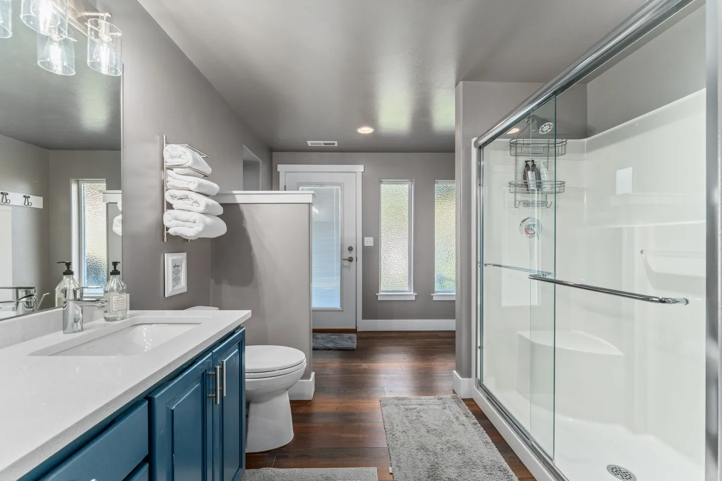 Bathroom featuring a blue vanity with a white countertop, toilet, and a glass-enclosed walk-in shower with a built-in seat.