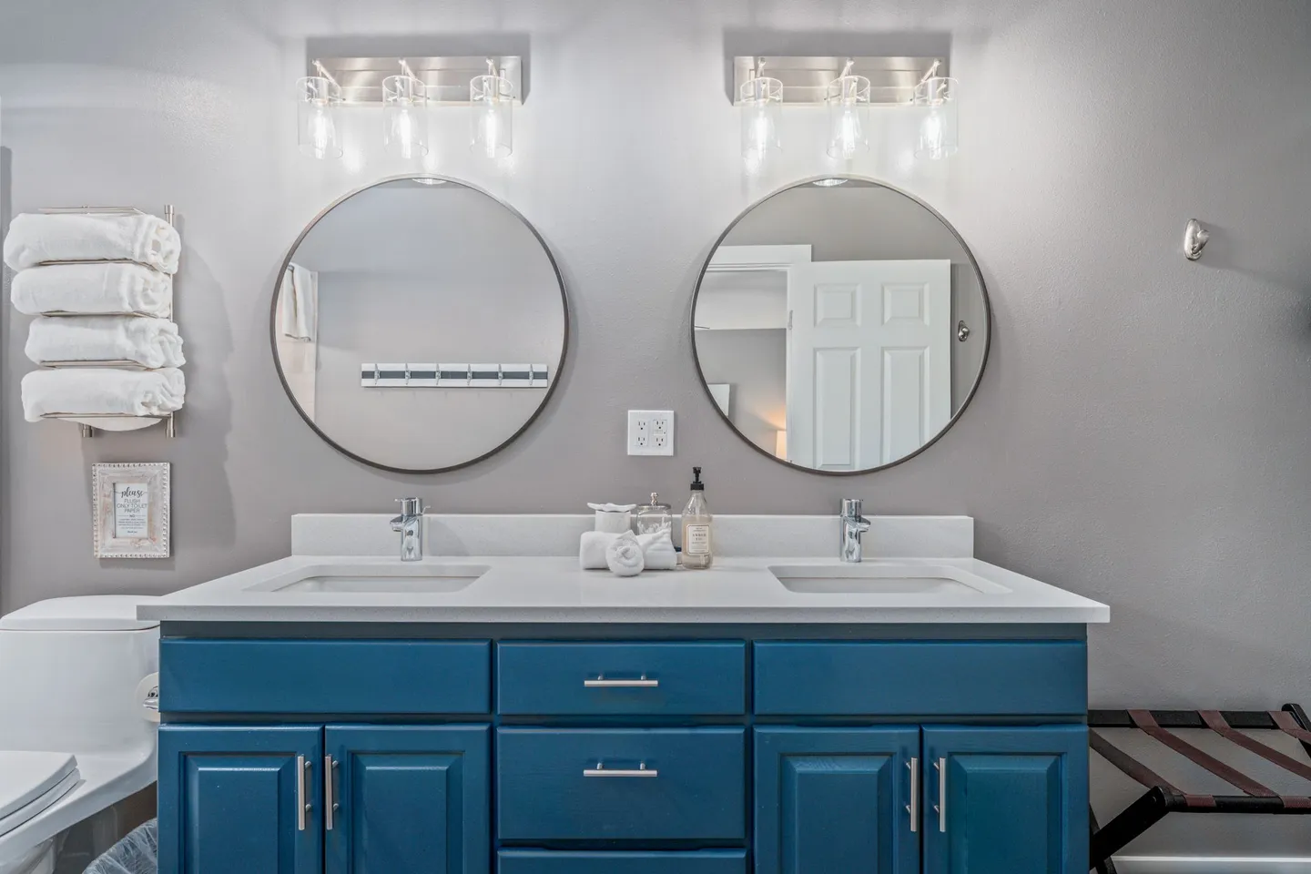 Bathroom double vanity with blue cabinetry, white countertop, two undermount sinks, and round mirrors.