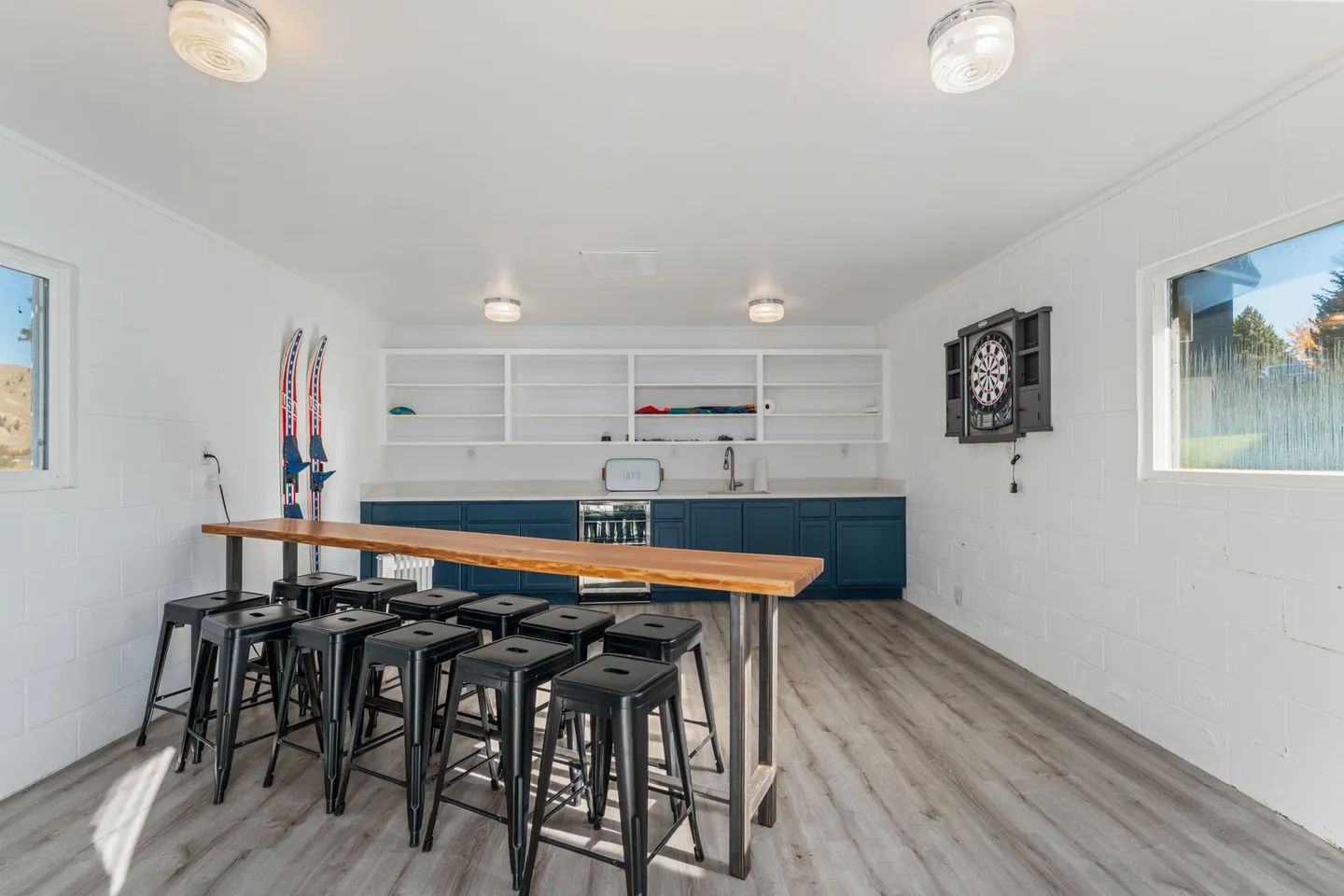 Rec room featuring a high-top wooden bar with black metal stools, a wet bar with blue cabinets and a beverage cooler, and a mounted dartboard.