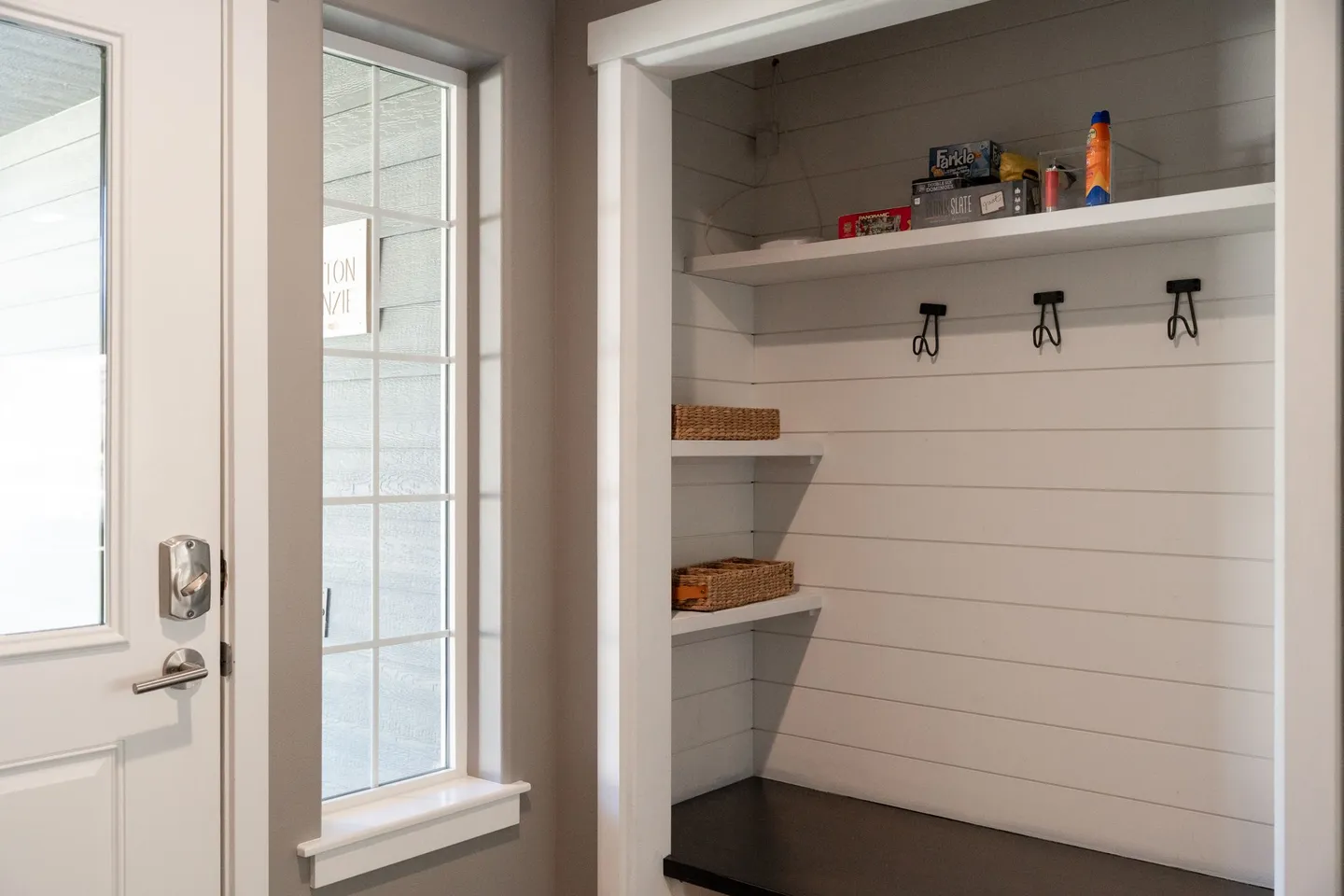 Entryway mudroom nook with built-in shiplap bench, coat hooks, shelves, and adjacent window next to the front door.