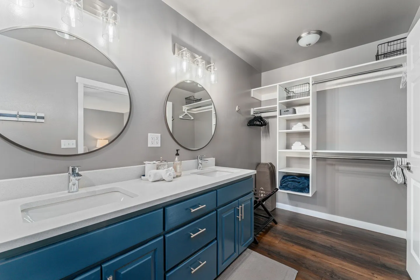 Bathroom with a double vanity featuring a blue cabinet, white countertop, two round mirrors, and an open closet area with white shelving.