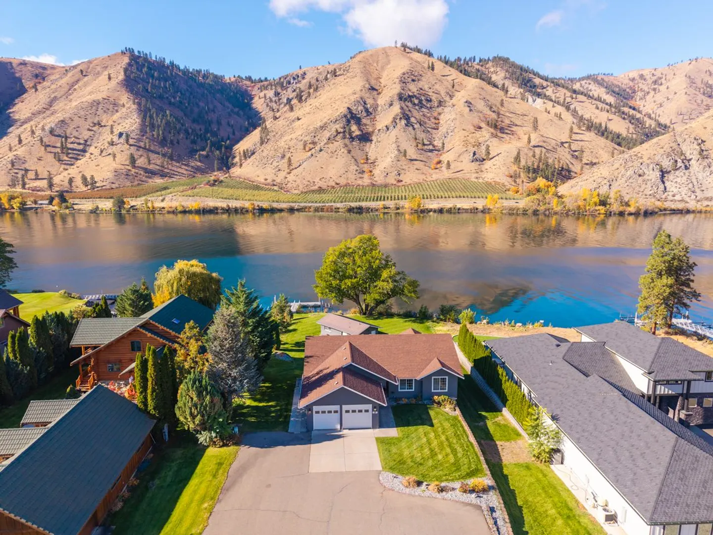 Aerial view of a waterfront home situated directly on a wide river with arid mountains rising on the opposite shore.